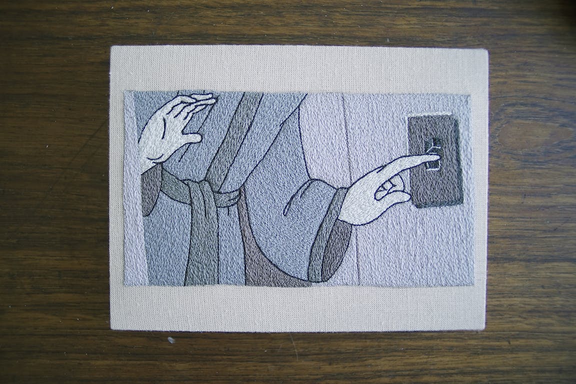 An embroidery shows a character in a night gown flipping a light switch.